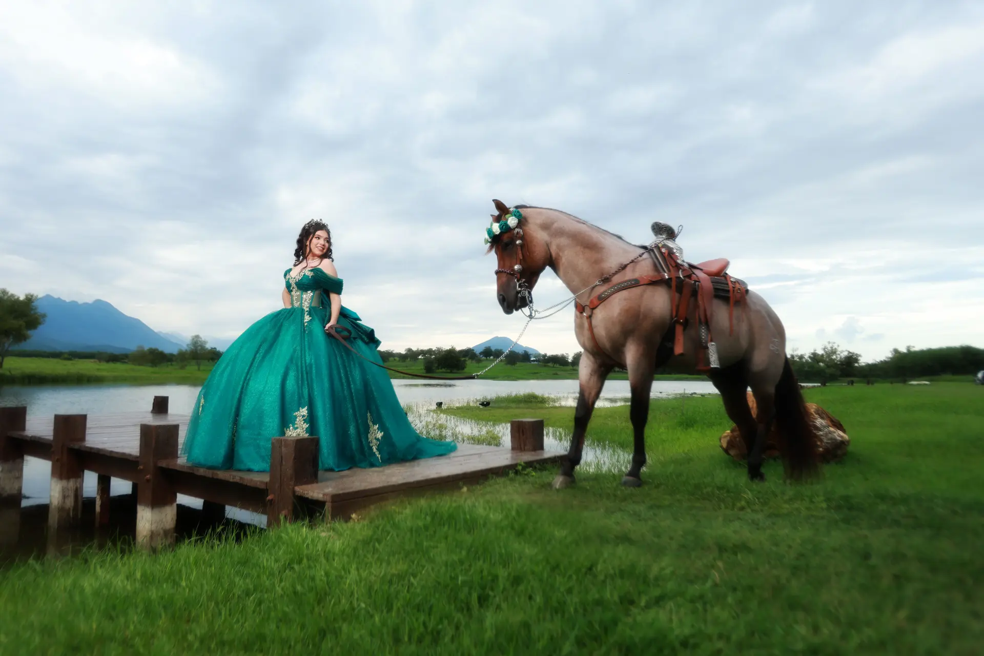 Quinceañera con vestido verde esmeralda junto a un caballo en un lago