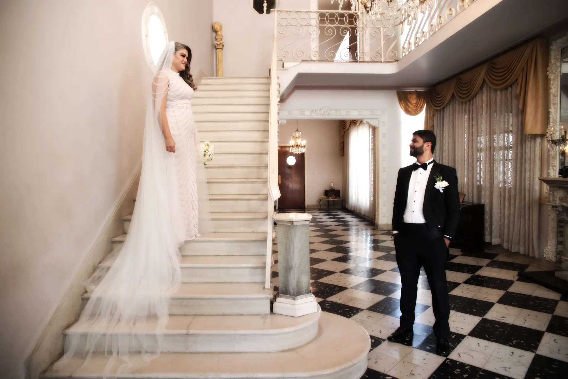 Novia con velo largo en una escalinata de mármol y el novio junto a ella