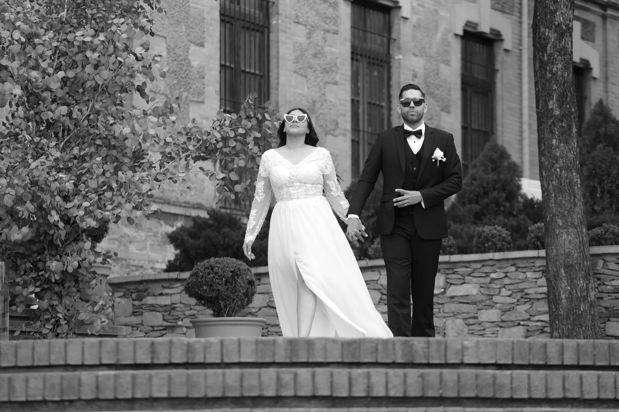 Pareja de novios caminando frente a una casona de piedra, en blanco y negro