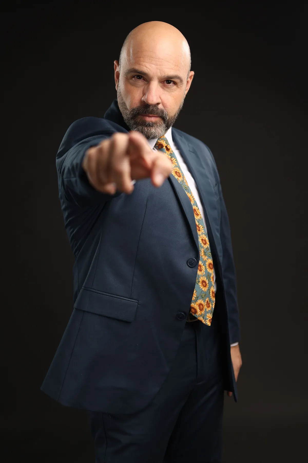 Hombre de traje azul señalando a la cámara sobre fondo oscuro