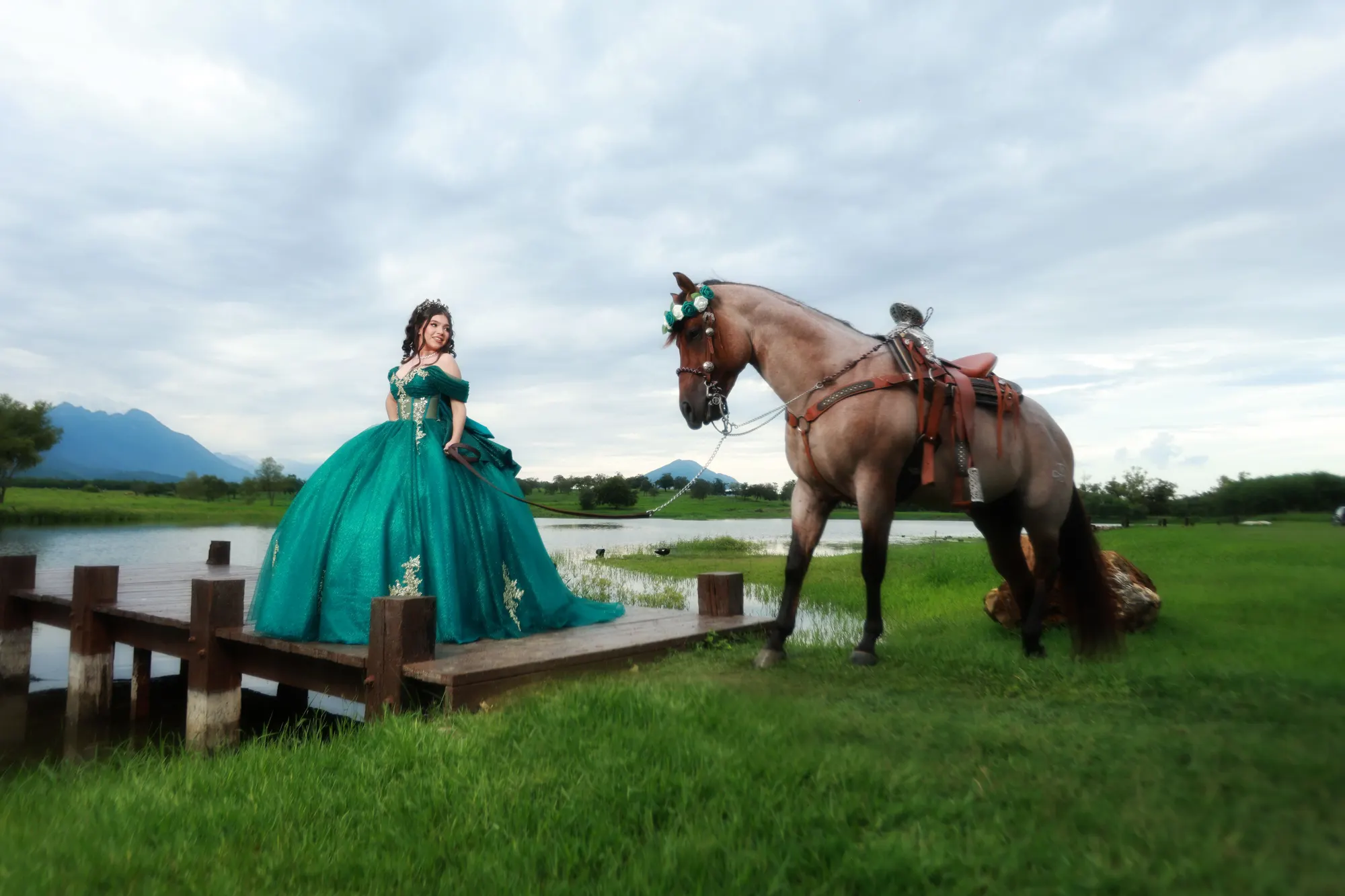 Quinceañera con vestido verde esmeralda junto a un caballo en un lago