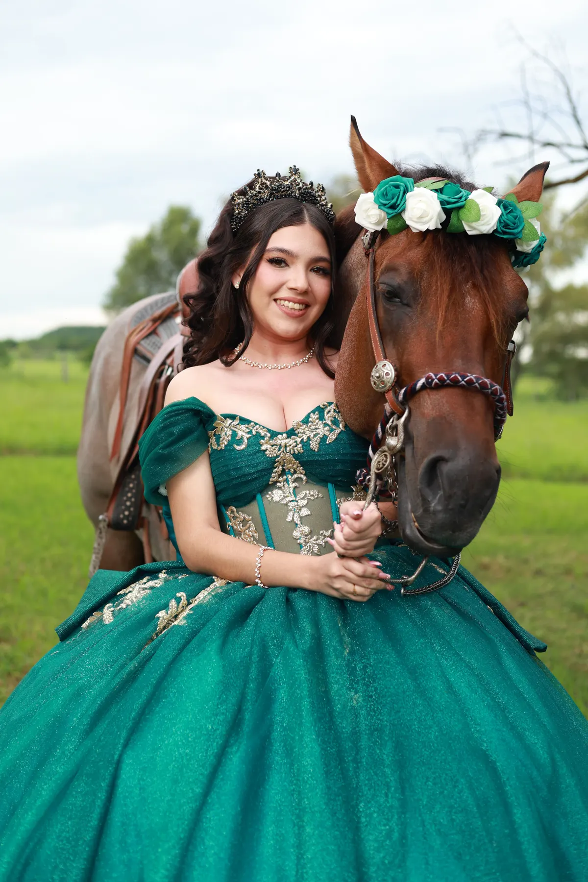 Quinceañera con vestido esmeralda y corona de flores junto a su caballo