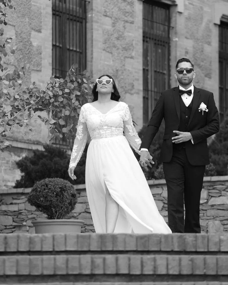 Pareja de novios caminando frente a una casona de piedra, en blanco y negro